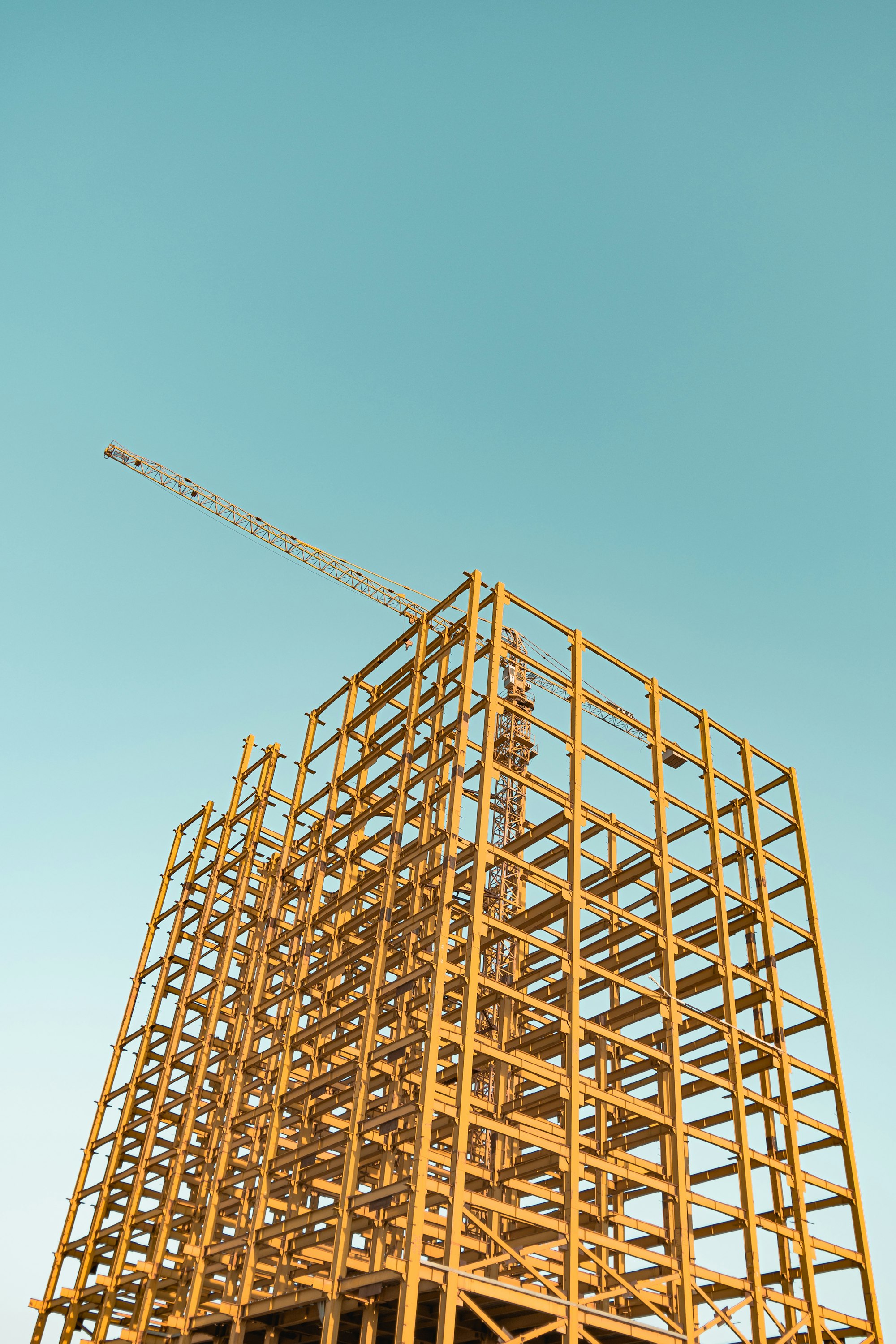 A building's exposed structural framework and a crane against a blue sky.